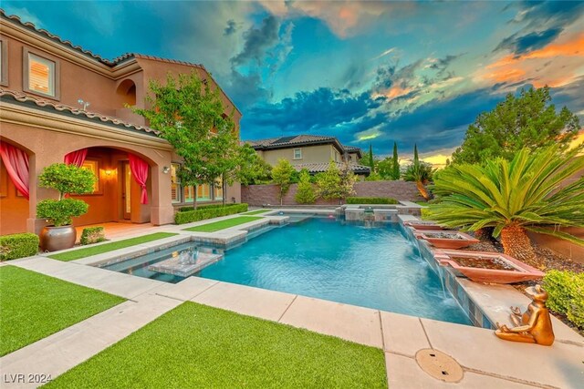 pool at dusk featuring an in ground hot tub and pool water feature