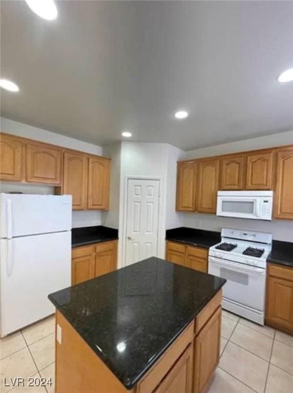 kitchen with dark stone countertops, a kitchen island, light tile patterned floors, and white appliances