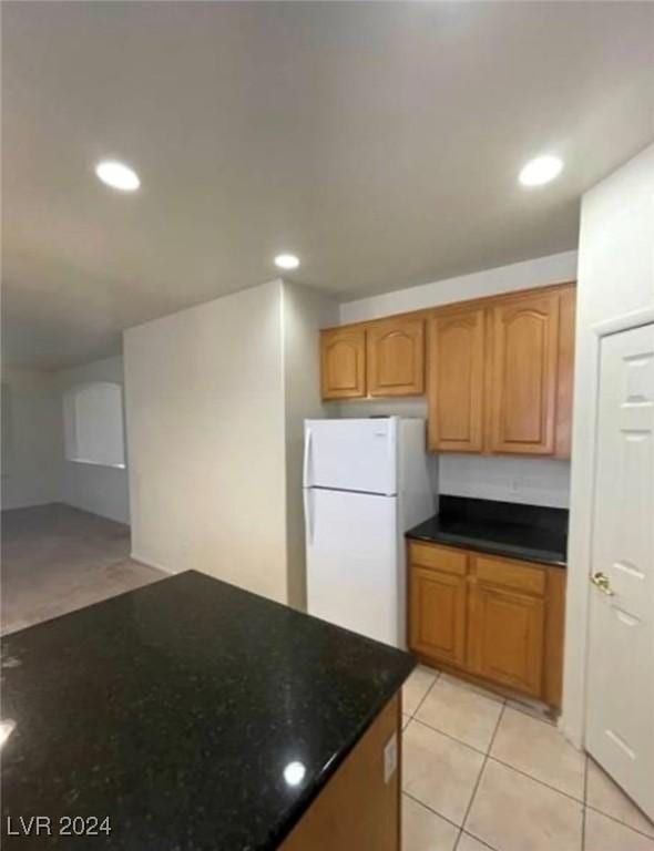 kitchen with dark stone countertops, light tile patterned flooring, and white refrigerator