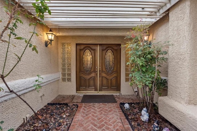 doorway to property featuring a pergola and stucco siding