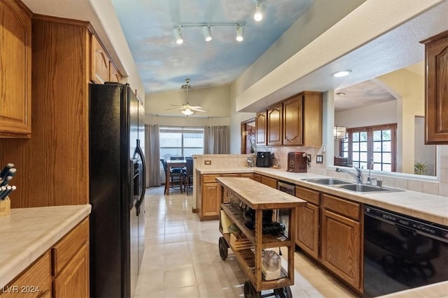 kitchen featuring tile countertops, brown cabinets, vaulted ceiling, black appliances, and a sink