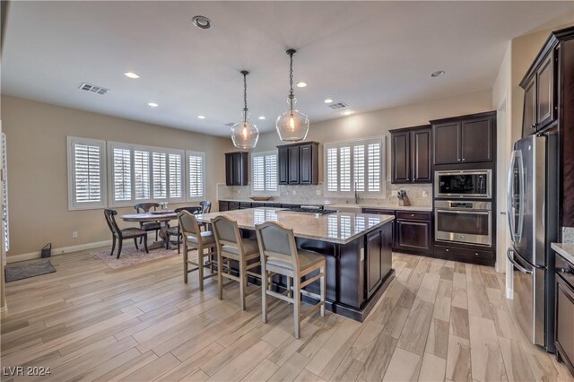 kitchen with light hardwood / wood-style flooring, backsplash, a center island, light stone counters, and appliances with stainless steel finishes