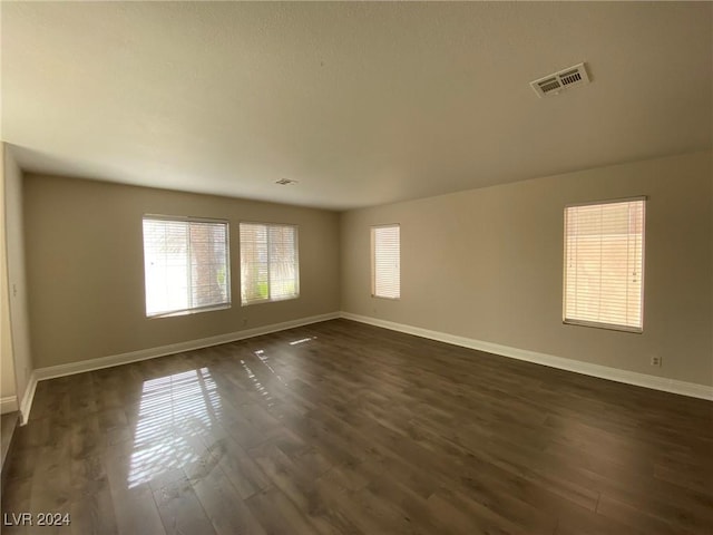 unfurnished room with baseboards, visible vents, and dark wood-type flooring