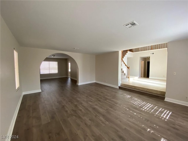 unfurnished living room featuring visible vents, baseboards, arched walkways, stairs, and dark wood-type flooring