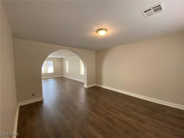 spare room with visible vents, baseboards, arched walkways, and dark wood-type flooring