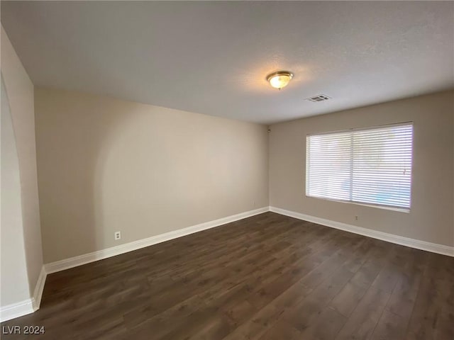 empty room with baseboards, dark wood-style floors, and visible vents