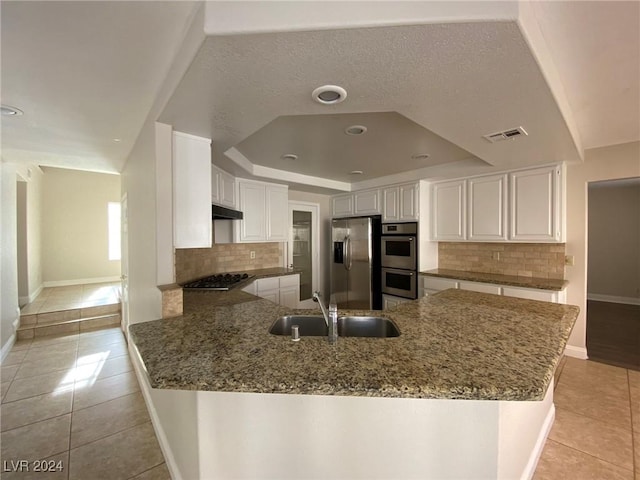 kitchen featuring appliances with stainless steel finishes, a raised ceiling, white cabinets, a sink, and a peninsula