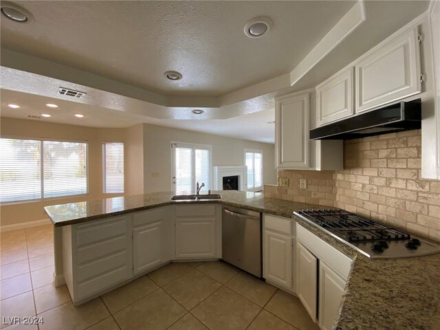 kitchen with kitchen peninsula, white cabinets, dark stone counters, a tray ceiling, and appliances with stainless steel finishes