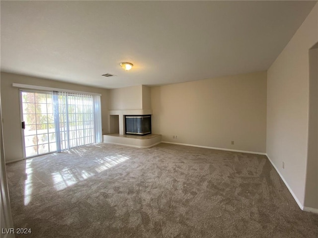 unfurnished living room with baseboards, a glass covered fireplace, and dark colored carpet