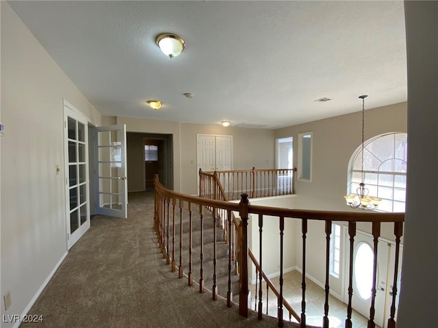 hall featuring baseboards, an inviting chandelier, dark colored carpet, an upstairs landing, and french doors