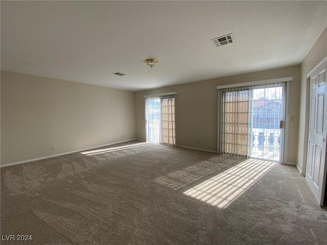 carpeted empty room featuring a wealth of natural light, baseboards, and visible vents