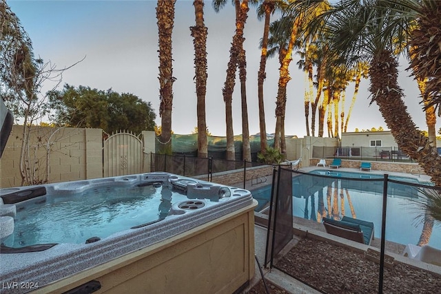 view of pool with a gate, fence, and a hot tub