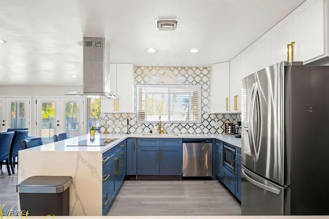 kitchen featuring white cabinets, a peninsula, blue cabinets, island exhaust hood, and stainless steel appliances