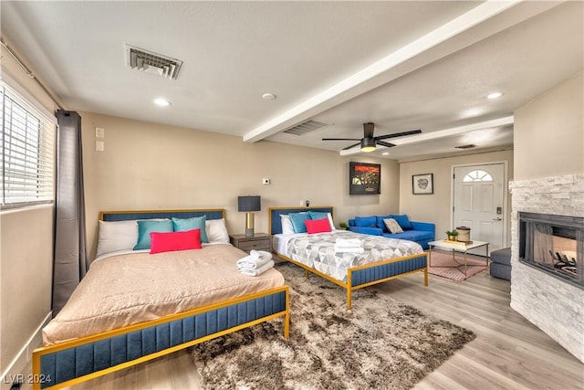 bedroom featuring light wood-type flooring, beam ceiling, visible vents, and a stone fireplace