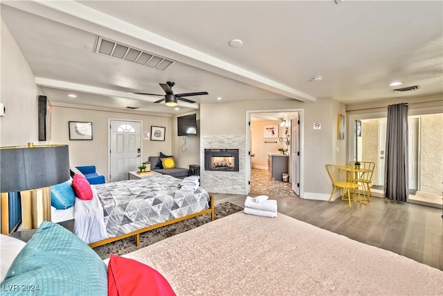 bedroom with a stone fireplace, multiple windows, dark wood finished floors, and visible vents