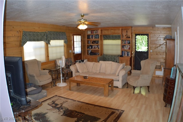 living room featuring ceiling fan, wooden walls, and light hardwood / wood-style floors