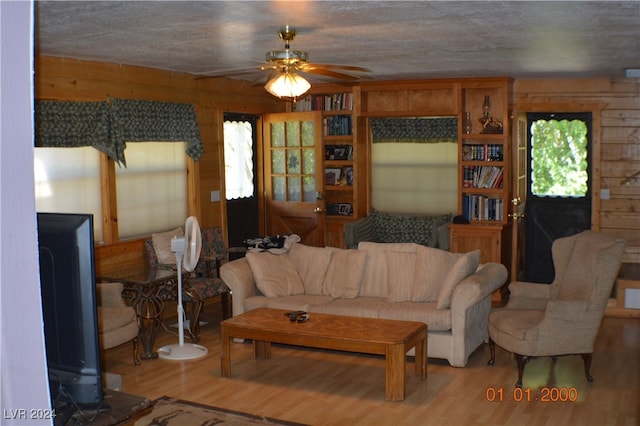 living room featuring ceiling fan, wood walls, and light hardwood / wood-style flooring