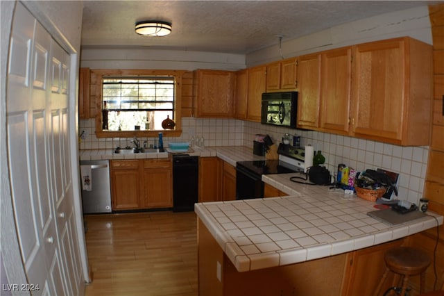 kitchen featuring black appliances, sink, kitchen peninsula, decorative backsplash, and tile counters