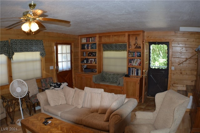 tiled living room featuring a textured ceiling, wood walls, and ceiling fan