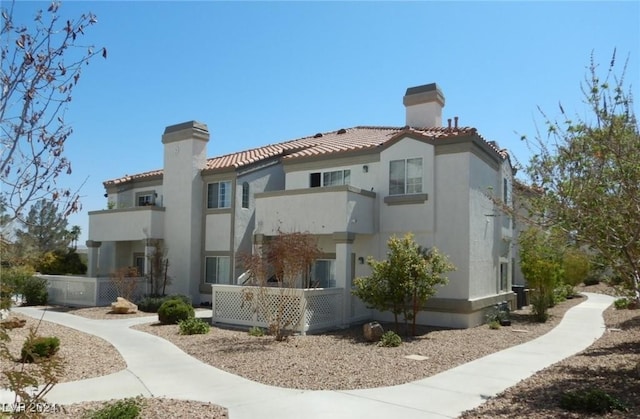 rear view of house with stucco siding, a chimney, and a tiled roof