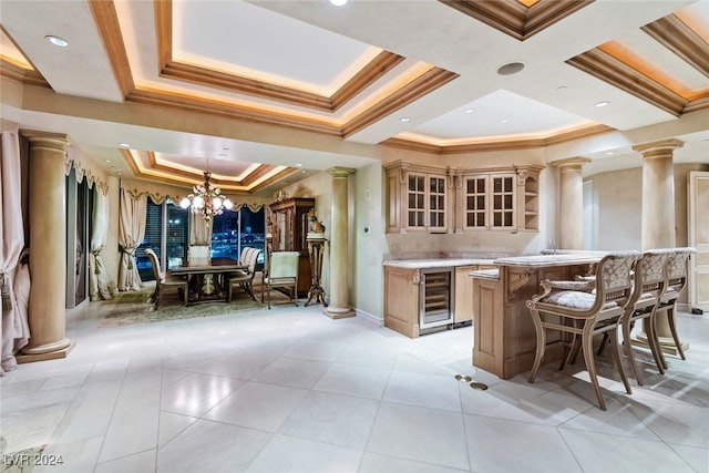 kitchen featuring an inviting chandelier, beverage cooler, decorative columns, a kitchen bar, and crown molding