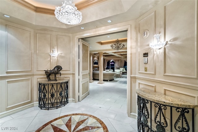 corridor with crown molding, light tile patterned floors, an inviting chandelier, a tray ceiling, and ornate columns