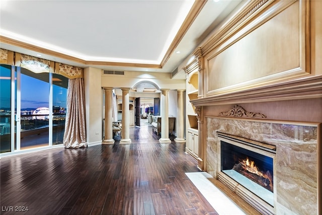 unfurnished living room featuring a premium fireplace, a tray ceiling, dark hardwood / wood-style flooring, and ornate columns