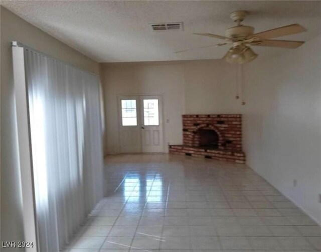 unfurnished living room featuring light tile patterned flooring, a brick fireplace, and ceiling fan