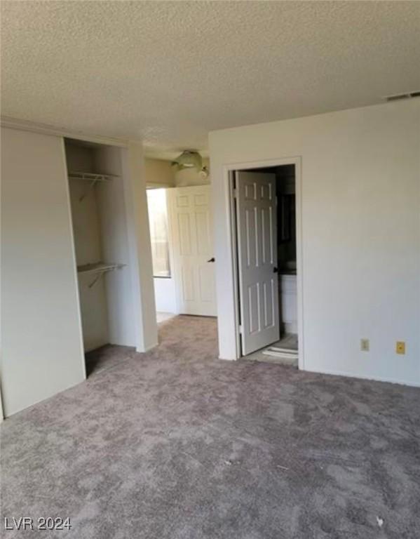 unfurnished bedroom with ensuite bath, a textured ceiling, and light colored carpet