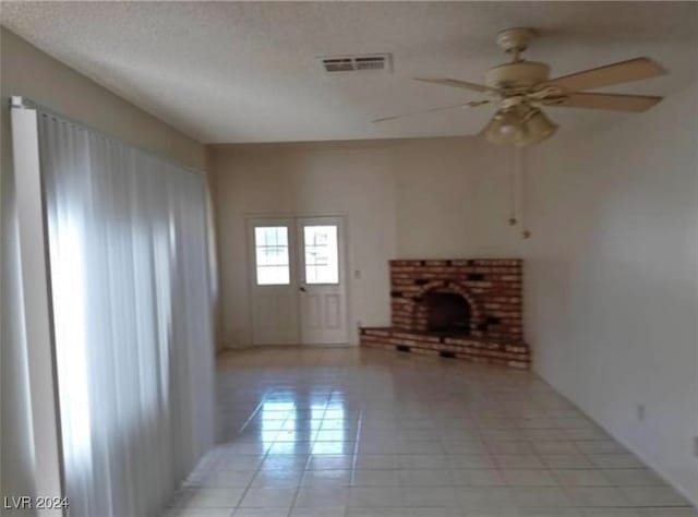 unfurnished living room featuring a textured ceiling, light tile patterned floors, a fireplace, and ceiling fan