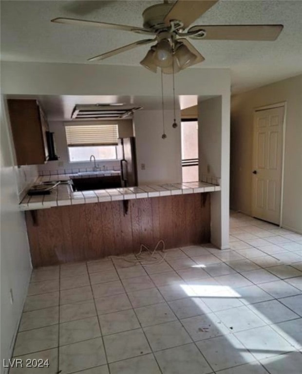 kitchen with light tile patterned flooring, kitchen peninsula, ceiling fan, and tile counters