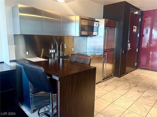 kitchen with paneled built in refrigerator, a peninsula, a breakfast bar, a sink, and stainless steel microwave