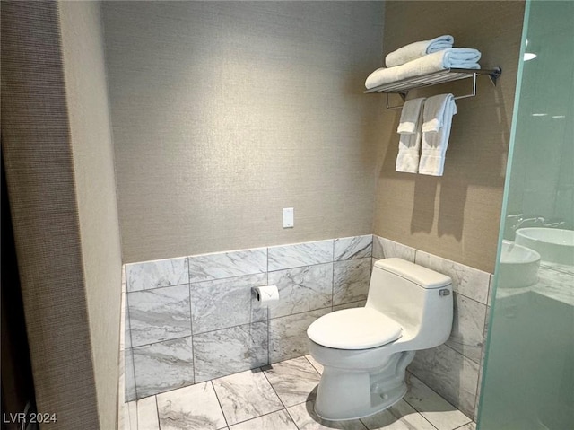 full bath featuring marble finish floor, toilet, and tile walls