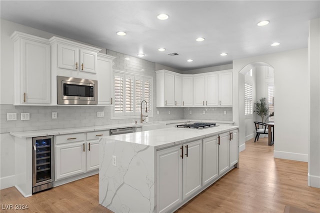 kitchen featuring stainless steel appliances, white cabinets, light stone counters, light hardwood / wood-style floors, and beverage cooler