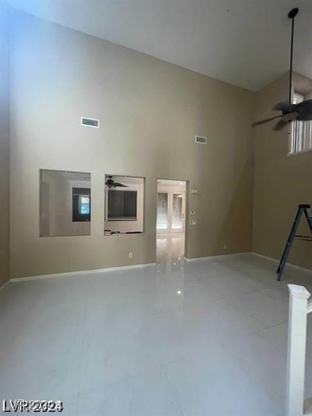 unfurnished living room with visible vents, a towering ceiling, a ceiling fan, and baseboards