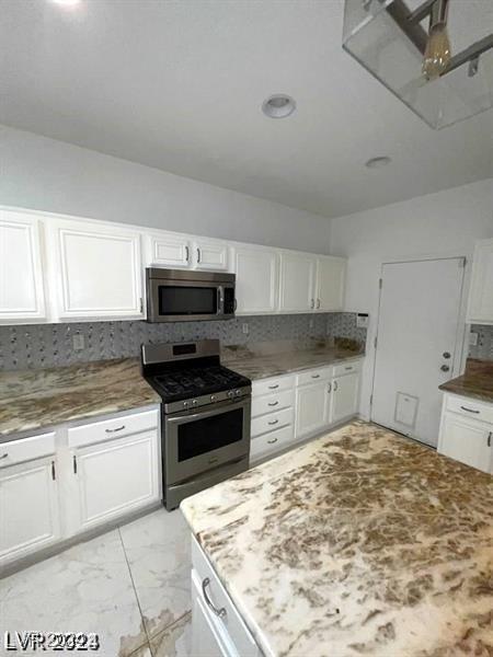 kitchen with decorative backsplash, light stone countertops, marble finish floor, stainless steel appliances, and white cabinetry