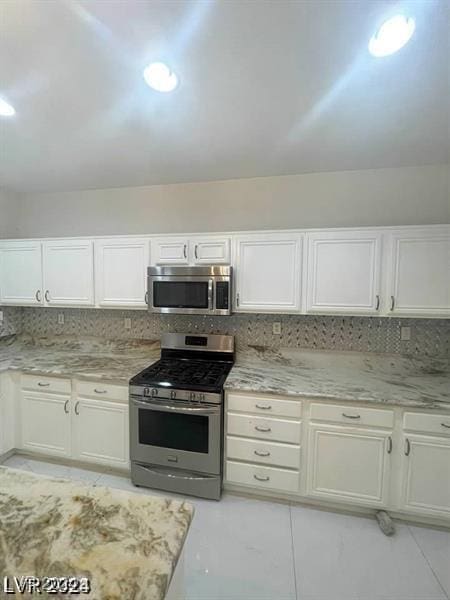 kitchen featuring decorative backsplash, appliances with stainless steel finishes, white cabinets, and light stone counters