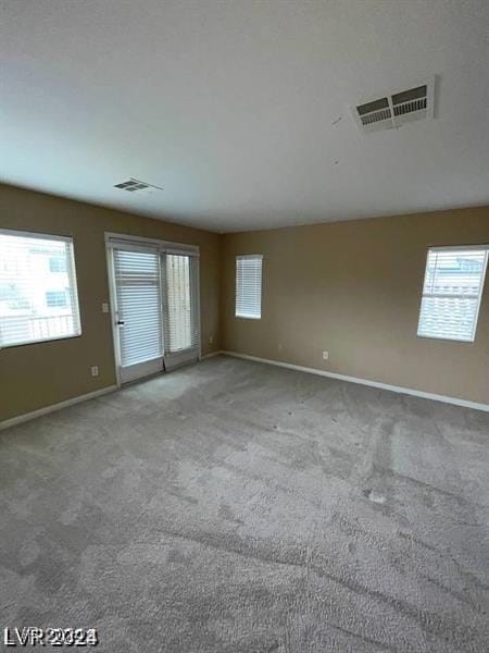 carpeted empty room featuring plenty of natural light, visible vents, and baseboards