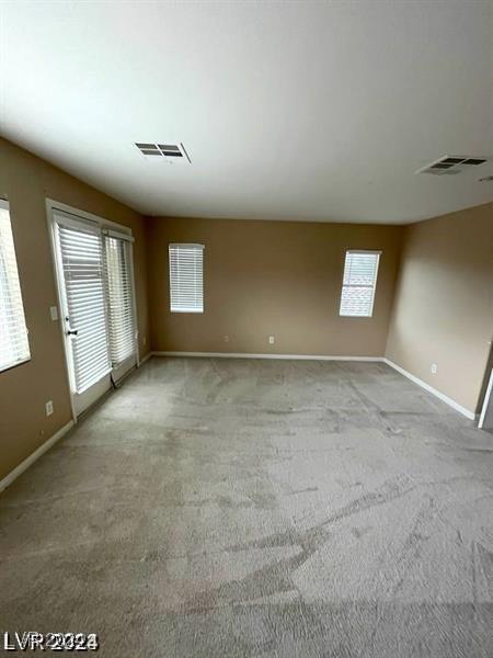 empty room featuring carpet floors, a healthy amount of sunlight, visible vents, and baseboards