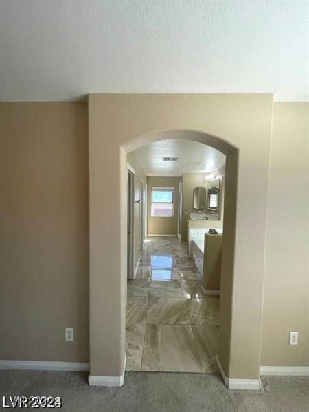 hallway featuring arched walkways, a textured ceiling, visible vents, and baseboards