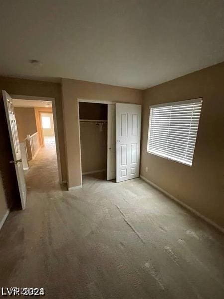 unfurnished bedroom with multiple windows, a closet, light colored carpet, and baseboards