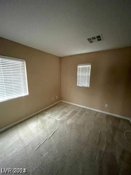 carpeted spare room featuring a wealth of natural light, visible vents, and baseboards