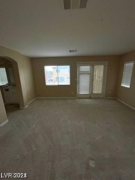 unfurnished living room featuring baseboards, visible vents, arched walkways, and light colored carpet