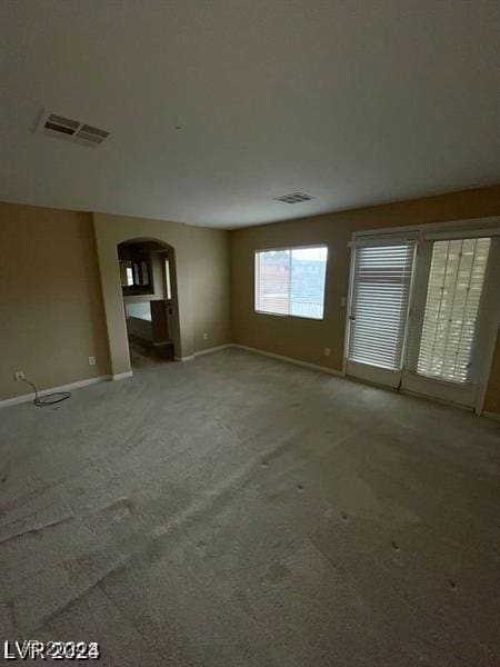 unfurnished living room with carpet floors, arched walkways, visible vents, and baseboards