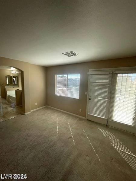 interior space featuring carpet floors, arched walkways, visible vents, and baseboards