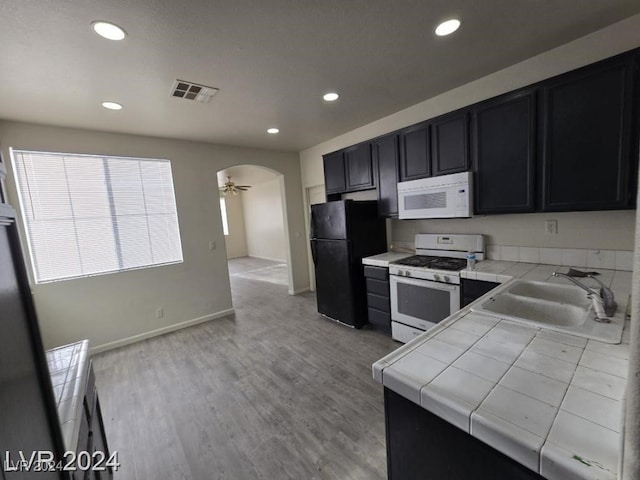 kitchen with visible vents, tile countertops, arched walkways, white appliances, and a sink