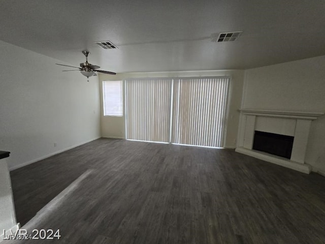 unfurnished living room with visible vents, a fireplace with raised hearth, wood finished floors, and a ceiling fan