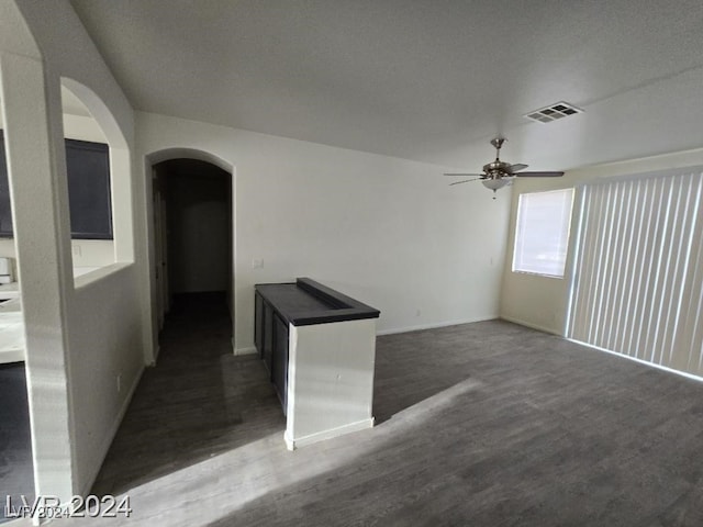 unfurnished room with a ceiling fan, dark wood-style floors, visible vents, and arched walkways