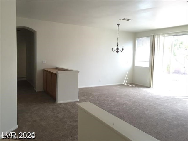 spare room featuring arched walkways, visible vents, dark carpet, and a notable chandelier