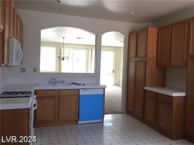 kitchen featuring tile counters, light floors, arched walkways, white appliances, and a sink